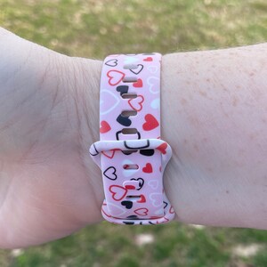 May include: A pink watch band with a pattern of red, white, and black hearts.