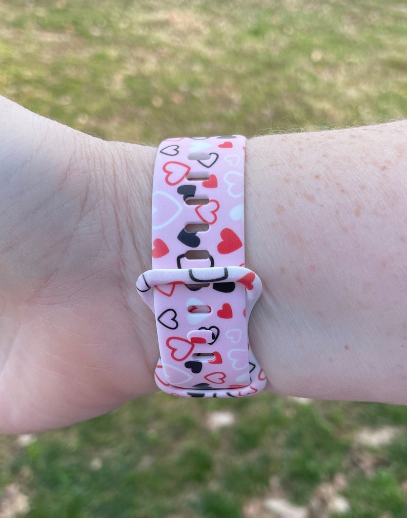May include: A pink watch band with a pattern of red, white, and black hearts.
