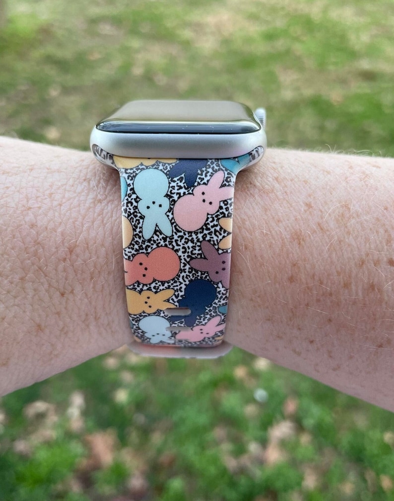 May include: A silver Apple Watch with a colourful patterned band featuring cartoon bunnies and a leopard print background.