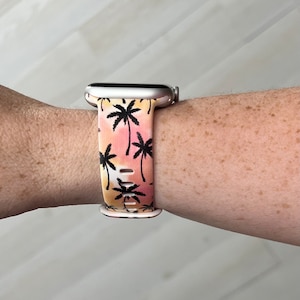 K&ouml;nnte beinhalten: Eine silberne Smartwatch mit einem pinkfarbenen und orangen Armband mit Palmenmuster.