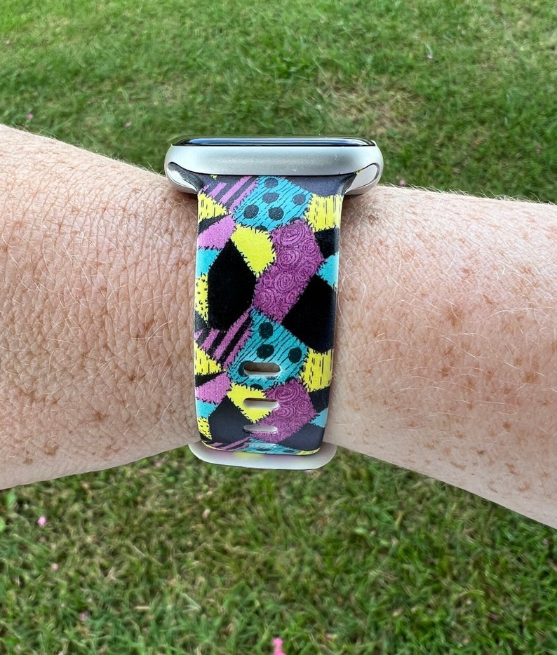 May include: A black, white, yellow, and purple patterned watch band with a silver watch face.