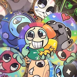 May include: A collection of colorful, round buttons featuring cartoon characters with various expressions. The buttons have a glossy finish and are decorated with hearts, stars, and rainbow patterns. The central button has a smiling face with rainbow-colored petals.
