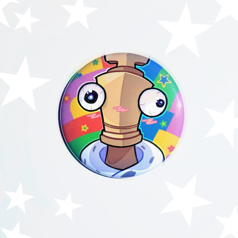 May include: A colorful button featuring a cartoon character with large eyes and a brown, gold, and white body. The character is wearing a white shirt with a blue collar and a red, yellow, green, and blue patterned background.