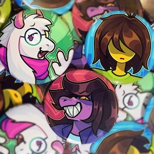 Pode incluir: Uma coleção de botões redondos e coloridos com ilustrações de personagens de desenhos animados. Os botões apresentam vários personagens com características distintas, incluindo uma figura branca semelhante a uma cabra com óculos e um cachecol rosa.