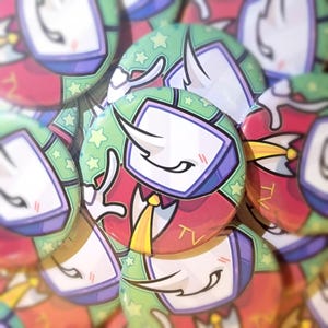 Puede incluir: Una colección de botones de solapa de estilo caricatura. Cada botón presenta un personaje con cabeza de pantalla de televisión, un cuerno blanco y un traje rojo con corbata amarilla. El fondo de algunos botones es verde con estrellas amarillas, y la palabra "TV" es visible.