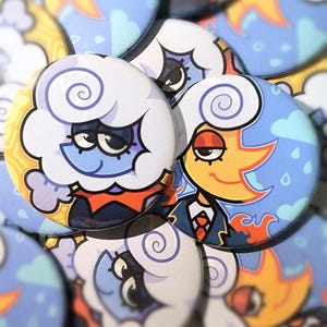 May include: A collection of round, cartoon-style buttons. The buttons feature illustrations of cloud and sun characters with expressive faces. The color palette includes blue, yellow, orange, and white, with a whimsical design. The buttons are likely for decorative purposes.
