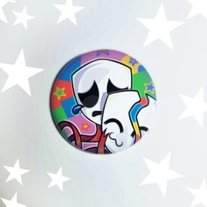 May include: A colorful button featuring two cartoon characters, one with a sad expression and the other with a happy expression. The characters are white with black eyes and mouths. The background is a colorful pattern of stars and stripes.