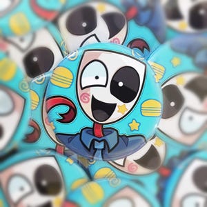 May include: A collection of round, cartoon-style buttons. The buttons feature a character with a white face, a large black eye, and a smiling mouth. The character is wearing a blue shirt and has a red neck. The background is light blue with yellow stars and burger icons.