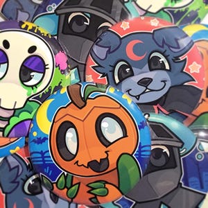 Pode incluir: Uma coleção de botões redondos e coloridos com ilustrações de desenhos animados. Os botões apresentam vários designs, incluindo uma abóbora, uma caveira e um lobo com uma lua crescente. Os botões são em tons de laranja, azul, verde e roxo.