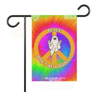 May include: A garden flag with a tie-dye design in pink, orange, green, and blue. It features a peace symbol with a white ghost character and the words "PEACE" and "DON'T BE A BOOLLY". The flag is printed on both sides.