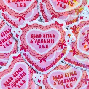May include: A collection of pink heart-shaped stickers with the text "READ SPICE & ABOLISH I.C.E." in a decorative font. The stickers have a scalloped edge and are adorned with bows.