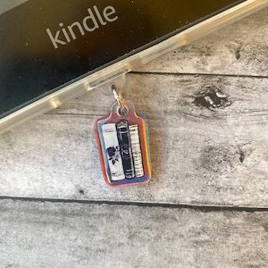 May include: A colorful book charm with a stack of three books, each with a different design. The charm is attached to a silver ring.