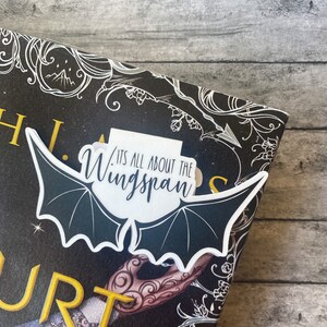 May include: A white bat-shaped bookmark with the text "It's all about the wingspan" on a black and white book cover with gold lettering.