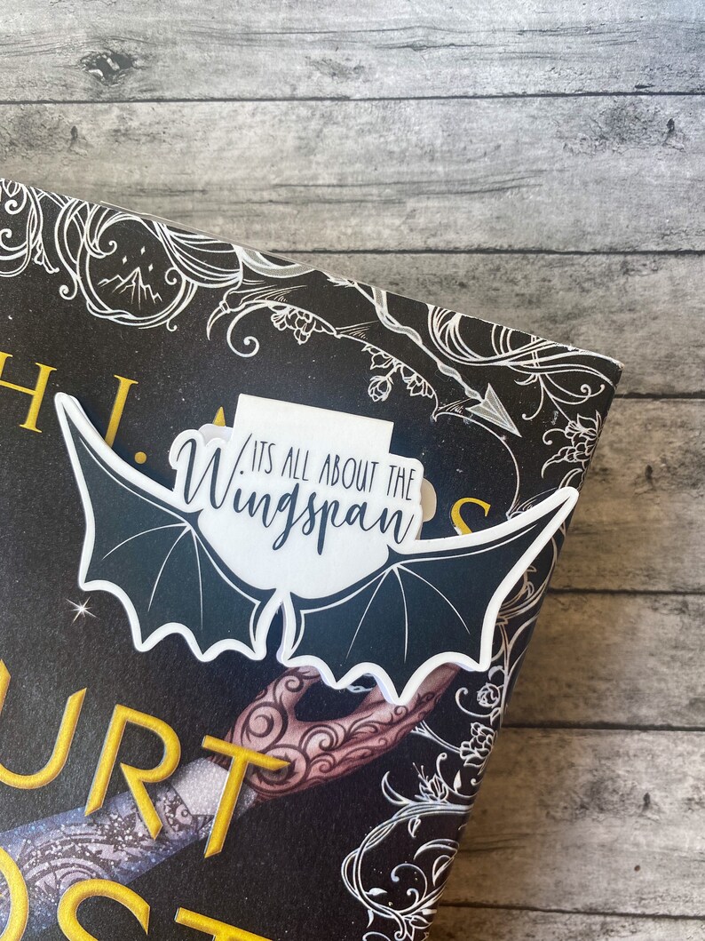 May include: A white bat-shaped bookmark with the text "It's all about the wingspan" on a black and white book cover with gold lettering.