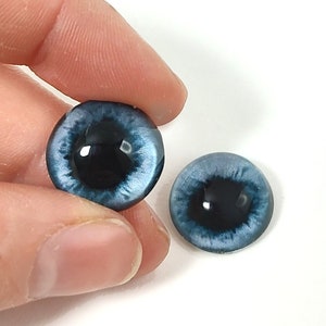 May include: Two blue glass eyes with black pupils, suitable for doll making or other craft projects.