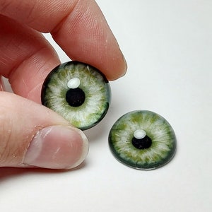 May include: Two green glass eyes with white pupils and black centers. The eyes are for doll making or other craft projects.