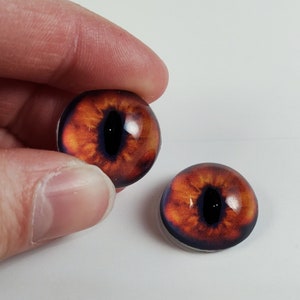 Op de afbeelding: Twee oranje glazen ogen met zwarte pupillen, geschikt voor het maken van poppen of andere knutselprojecten.