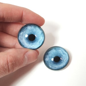 May include: Two blue glass eyes with black pupils and white irises. The eyes are round and have a realistic appearance.