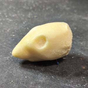 May include: A light yellow, textured object shaped like a bird's head, with a small, round hole near the eye area. The beak is pointed, and the overall form is smooth with a slightly rough surface.
