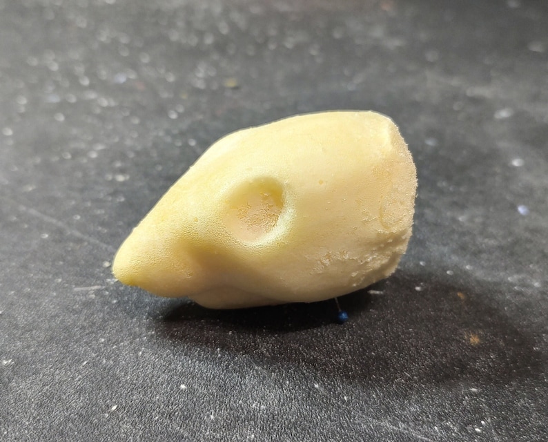 May include: A light yellow, textured object shaped like a bird's head, with a small, round hole near the eye area. The beak is pointed, and the overall form is smooth with a slightly rough surface.