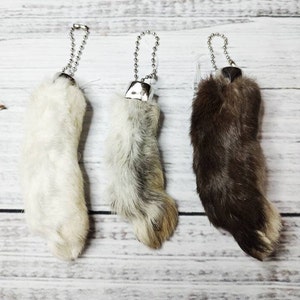 May include: Three rabbit foot keychains with silver chains. The rabbit feet are white, gray, and brown.
