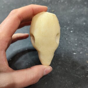 May include: A light yellow, oblong-shaped object with two circular indentations, held in a hand against a dark background. The object has a smooth texture and a rounded base, resembling a stylized form.