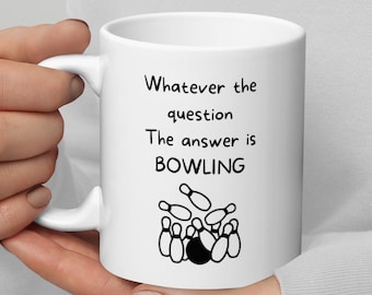 Pode incluir: Caneca de cerâmica branca com uma ilustração em preto e branco de pinos de boliche e uma bola de boliche. O texto na caneca diz "Whatever the question The answer is BOWLING".