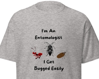Può includere: Una maglietta grigia con il testo "I'm an Entomologist I Get Bugged Easily" e illustrazioni di tre insetti.