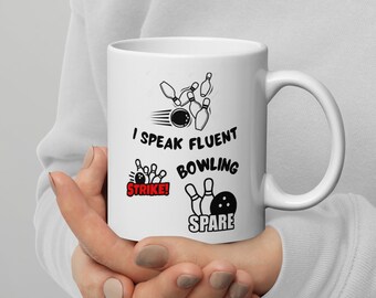 Pode incluir: Caneca de cerâmica branca com um design de boliche em preto e branco. A caneca diz "Falo boliche fluentemente" com um gráfico de strike e spare.