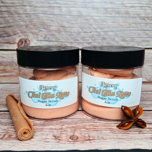 May include: Two glass jars of orange-colored sugar scrub with black lids. The jars are labeled "Lavery Chai Tea Latte Sugar Scrub 4oz".