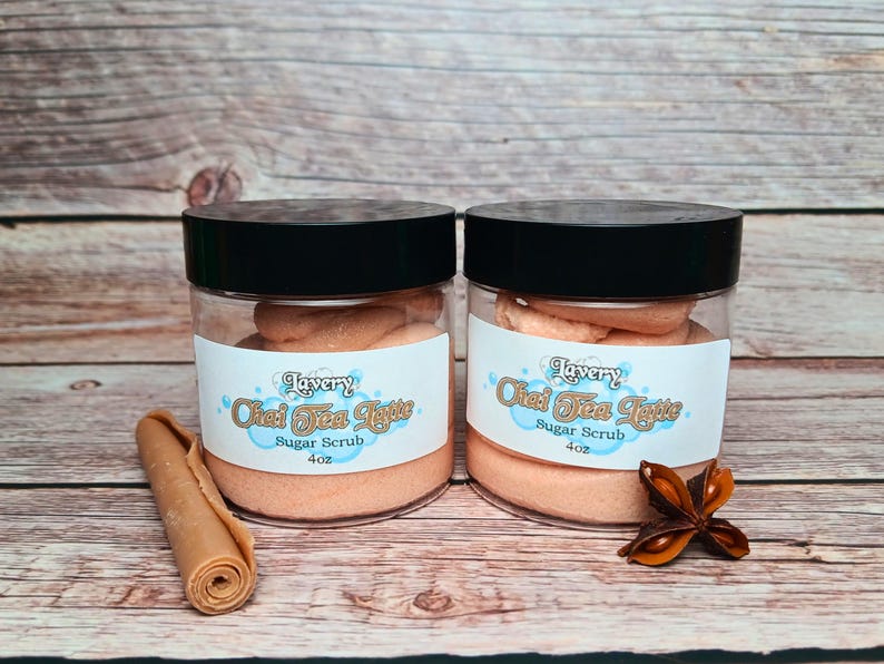 May include: Two glass jars of orange-colored sugar scrub with black lids. The jars are labeled "Lavery Chai Tea Latte Sugar Scrub 4oz".
