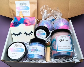 May include: A gift box filled with unicorn-themed bath and body products. The box includes a bath bomb, a sugar scrub, a body butter, a soy candle, and a bath soak. The products are all packaged in clear jars with labels that say "Lavery Unicorn".