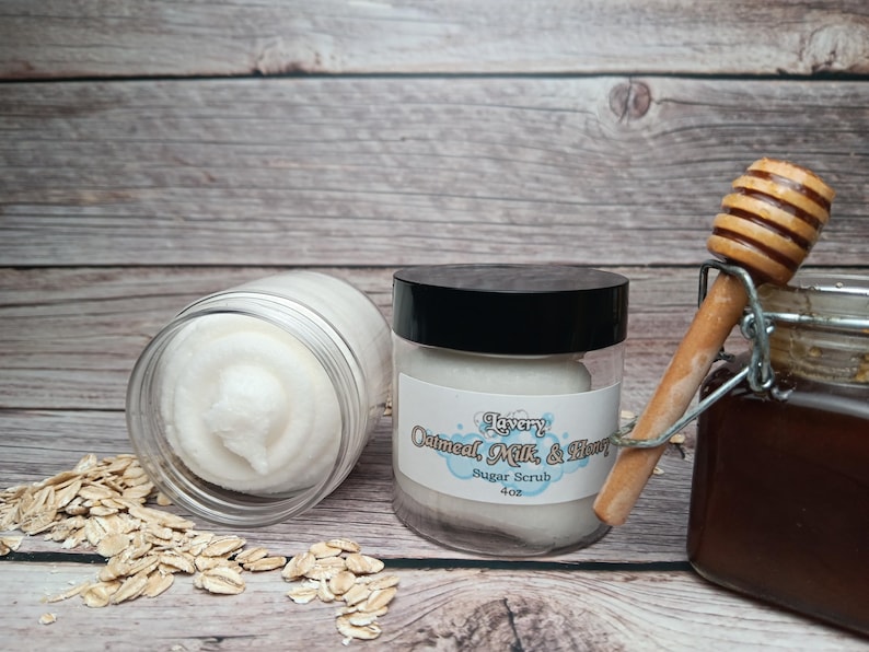 May include: Two glass jars of oatmeal, milk, and honey sugar scrub. The jars are on a wooden surface with a scattering of oatmeal. The label on the jar reads "Lavery Oatmeal, Milk, & Honey Sugar Scrub 4 oz."