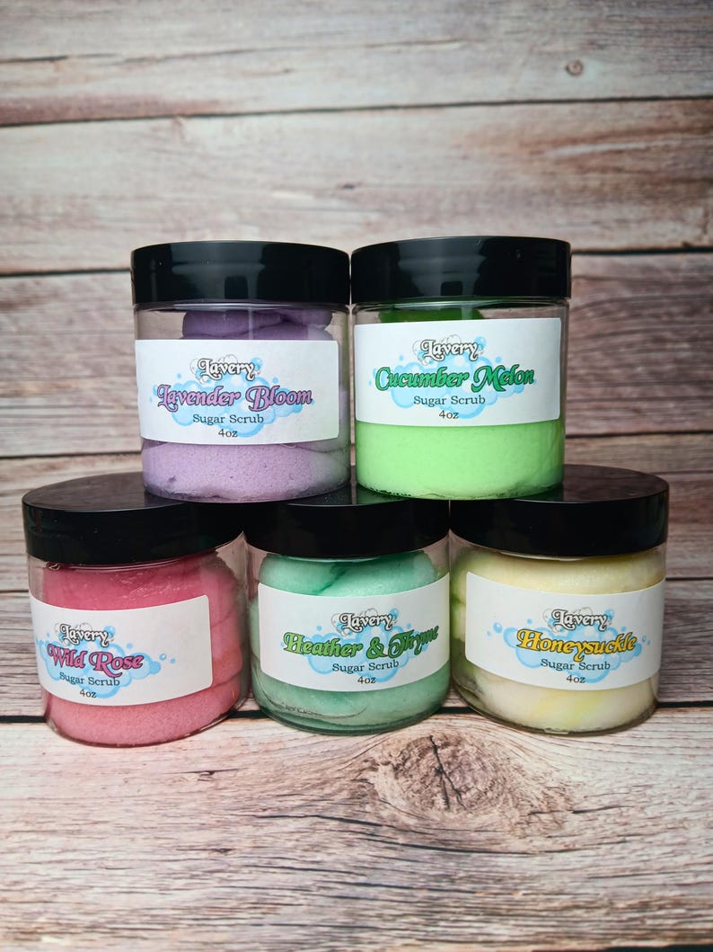May include: Five glass jars with black lids filled with colorful sugar scrubs. The labels on the jars read "Lavery" and list the scents: Lavender Bloom, Cucumber Melon, Wild Rose, Heather & Thyme, and Honeysuckle. Each jar is 4 oz.