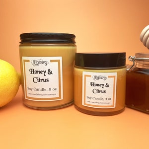 May include: Two glass jars of soy candles labeled "Honey & Citrus", 8 oz and 4 oz, with black lids. A lemon and a jar of honey with a wooden honey dipper are also present. The candles have a light orange background.