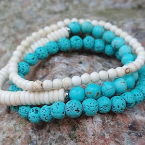 May include: Three stacked bracelets featuring turquoise and cream-coloured beads. The turquoise beads have a textured finish, and the cream beads are smooth. The bracelets are presented on a textured, grey stone surface.