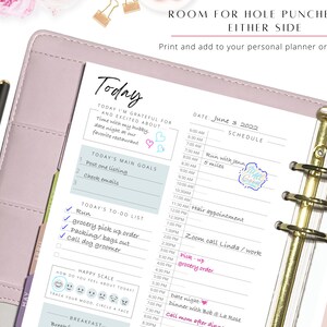 May include: A pink and white daily planner with a gold binder ring. The planner has a daily schedule, a to-do list, and a mood tracker. The date is June 3, 2022. The text "Room for hole punches on either side" is at the top of the page.