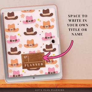 May include: A white planner with a brown leather cover and a pink and brown cowboy hat pattern. The cover has a brown leather label with the text "No. PLANNER" on it. The planner has a space to write in your own title or name.