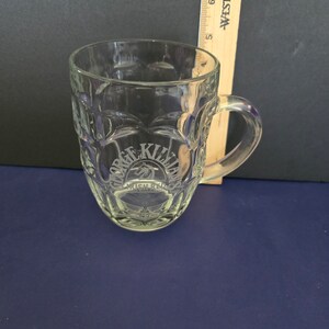 May include: A clear glass pint glass with a raised design and a handle. The glass has the words "George Killian's Irish Red" etched into the side.