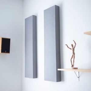 May include: Two gray acoustic panels mounted on a white wall, a wooden speaker on the wall, a wooden shelf with books and a wooden figurine on top.