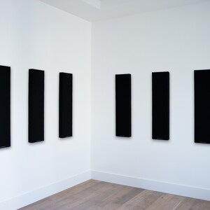 May include: Six black acoustic panels mounted on a white wall. The panels are rectangular and vertical.