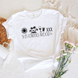 May include: White t-shirt with a black graphic design featuring a sun, palm trees, wine glass, beer glass, and the text "XXX Si es contigo mejor".