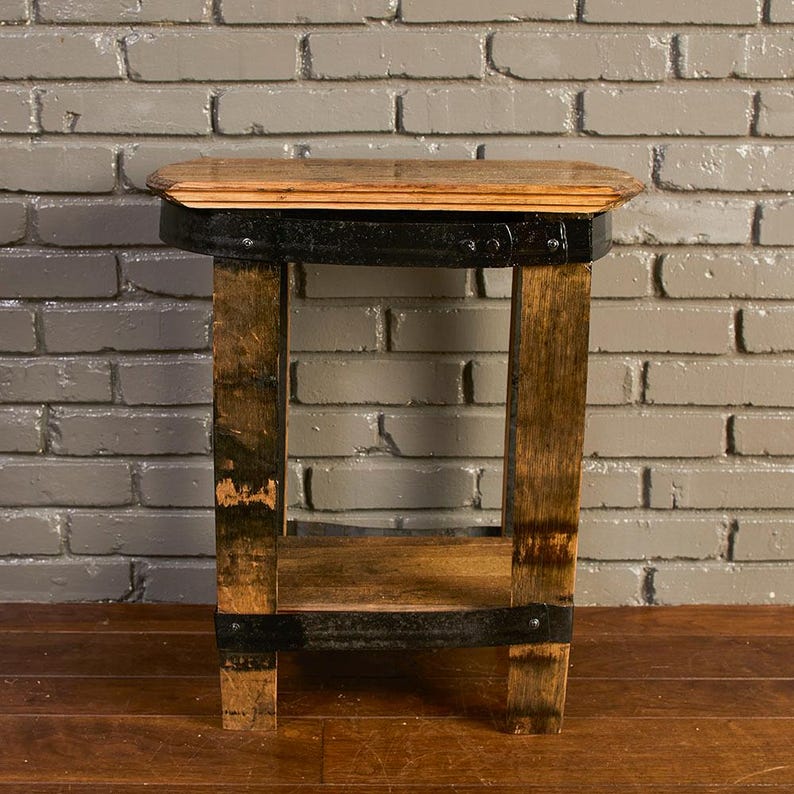 Op de afbeelding: Een bijzettafel gemaakt van gerecyclede houten vaten, voorzien van een glad lichtbruin houten blad, vier verticale poten en een onderste plank, versterkt met donkere zwarte metalen banden met zichtbare klinknagels.