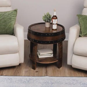 May include: A round side table constructed from a dark brown wooden barrel with black metal bands. The table features a flat top surface, a lower shelf holding two white books, and a sturdy base. A bottle of Basil Hayden bourbon sits on top.
