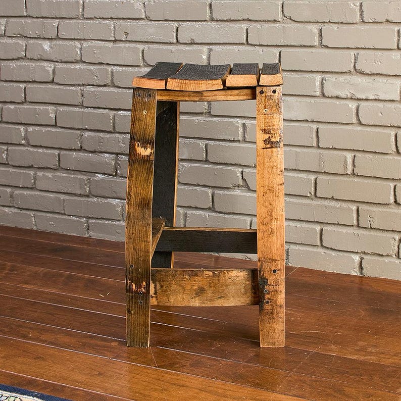 May include: A stool constructed from reclaimed wooden barrel staves, featuring a curved seat made of four parallel dark-stained wood planks and four vertical legs reinforced with horizontal crossbars, showcasing natural wood grain and charred textures.