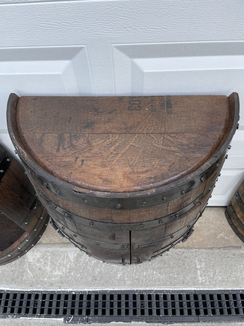 May include: A half-barrel wooden cabinet with two doors. The cabinet is made of dark brown wood and has metal bands around the edges. The top of the cabinet is flat and has a label that reads '800'. The cabinet is sitting on a concrete surface with a black drain grate in the foreground.