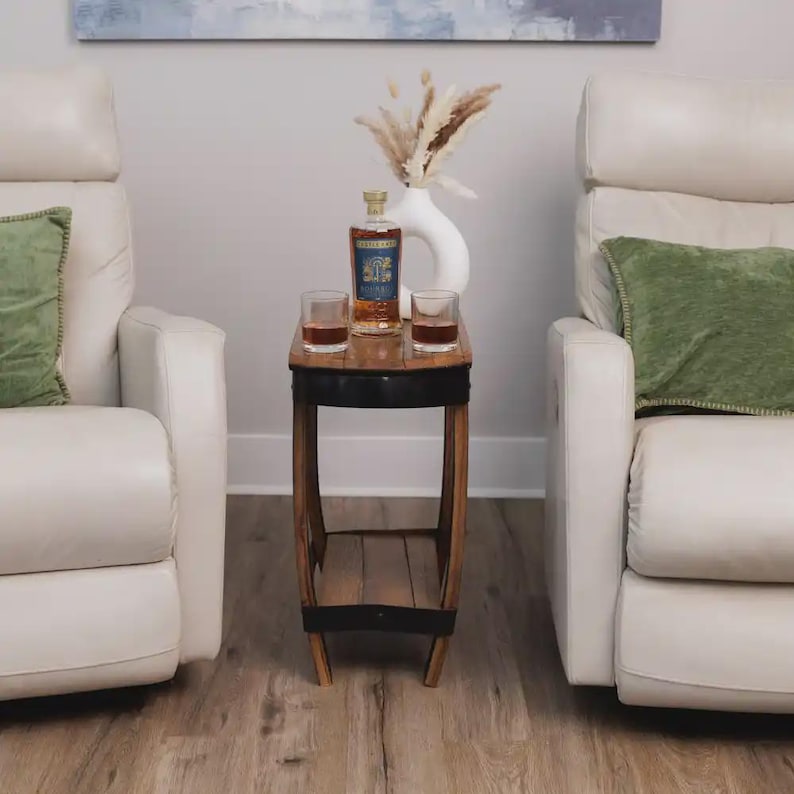 Op de afbeelding: Een houten bijzettafel met een donkere metalen band, waarop een glazen fles Castle & Key bourbon, twee heldere glazen gevuld met amberkleurige vloeistof en een witte keramische vaas met gedroogde beige pampasgraspluimen staan.
