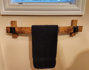 May include: A wooden towel rack with black metal accents, mounted on a wall. A dark blue towel is hanging on the rack.