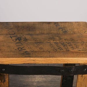 Op de afbeelding: Een kleine kruk gemaakt van een gerecyclede houten ton, met een natuurlijke eikennerf afwerking en een donkere metalen band rondom de zitting. Het bovenoppervlak toont zwarte gestencilde tekst met BARDSTOWN en andere markeringen.