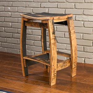 May include: A stool constructed from reclaimed oak wood barrel staves, featuring a curved seat and four legs connected by horizontal support braces. The wood displays natural grain patterns, light brown tones, and dark charred charcoal accents.